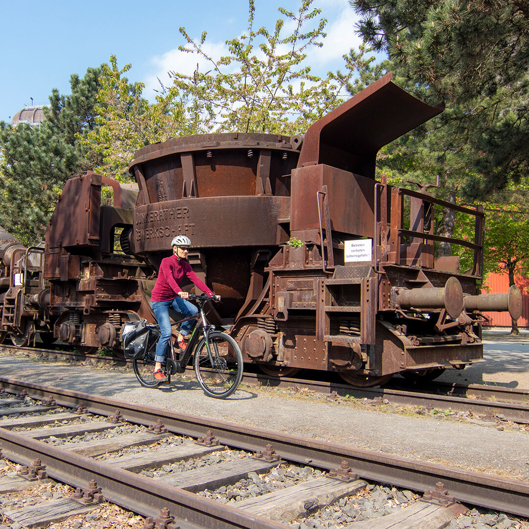 Eine Frau fährt mit dem E-Bike an einem alten, stillgelegten Zug vorbei